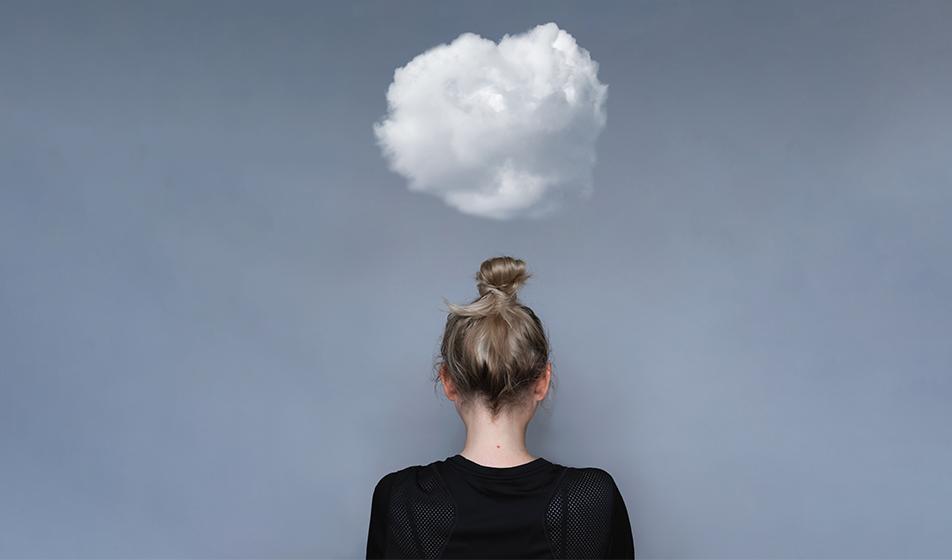 A woman with her hair in a bun facing away from the camera, towards a storm-coloured dark grey wall. There's a small white cloud hovering directly over her head. 