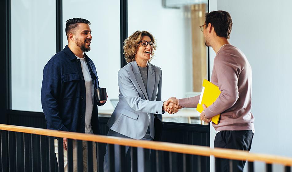 Two colleagues shake hands with a new employee, smiling