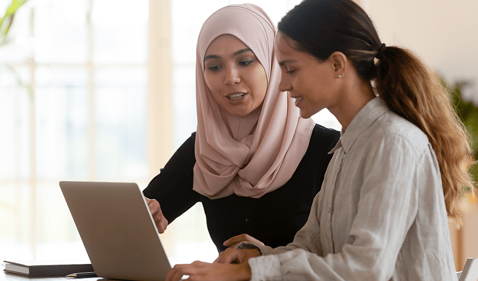 A woman sat helping her apprentice. They are working on a laptop together.