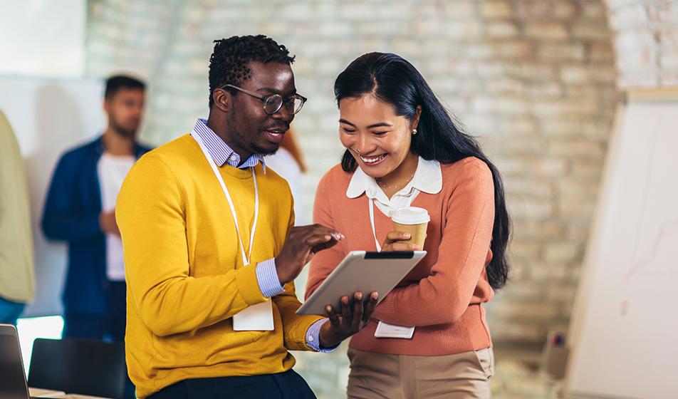 A man and a woman look at an ipad in an office environment. They appear to be communicating happily. 