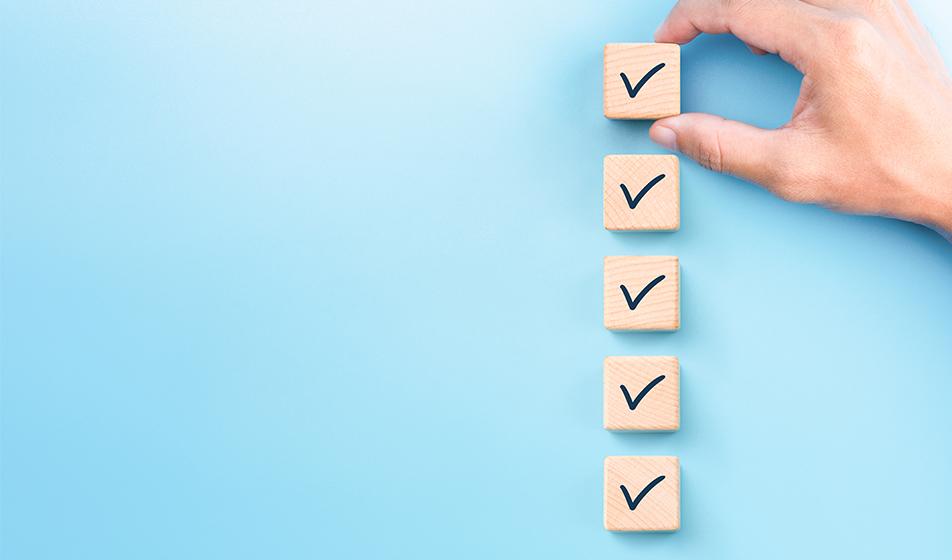 5 wooden cubes are shown, stacked on top of each other on the right of the image, against a plain blue background. There are ticks on each of the cubes, and a hand adjusts the top one.