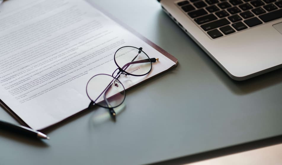 Glasses resting on paperwork next to a laptop on a desk