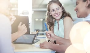 A woman smiling at her colleague as they work around a desk together.