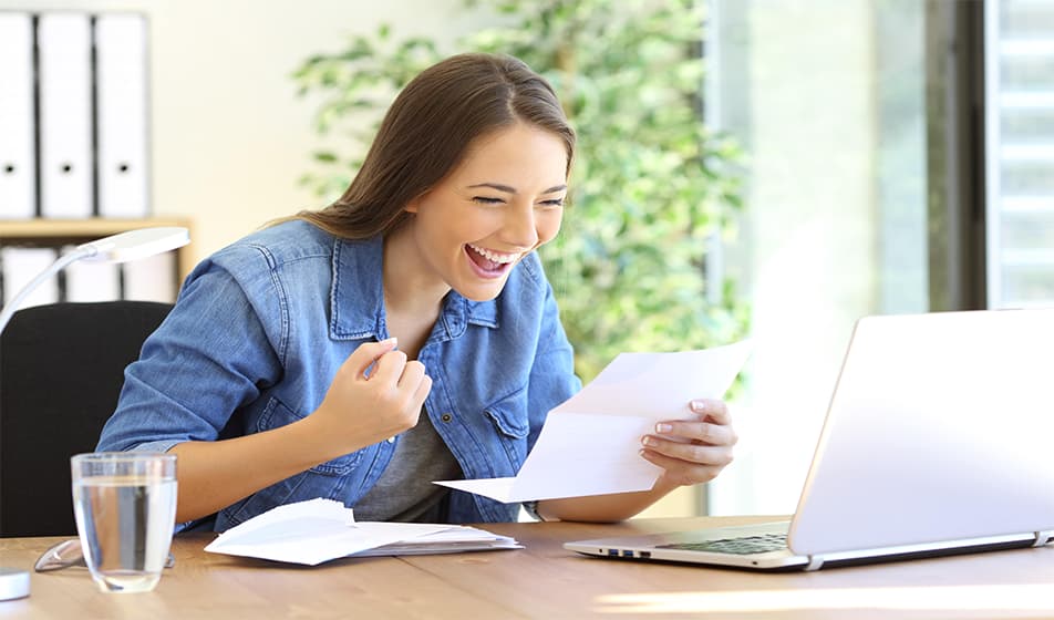 Lady celebrating while holding a letter sitting down at her desk