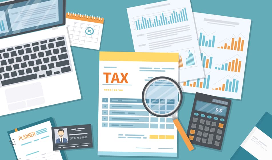 A cartoon showing tax documents and a laptop sat on a blue desk surrounded by a calculator and various graphs.