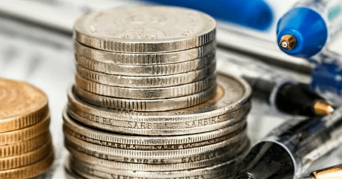 Two piles of coins are stacked next to each other. They are surrounded by black and white pens.